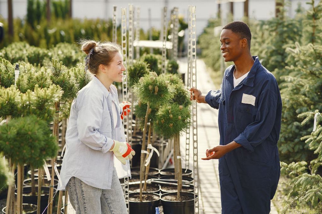 A gardener in overalls talking with a customer among potted plants