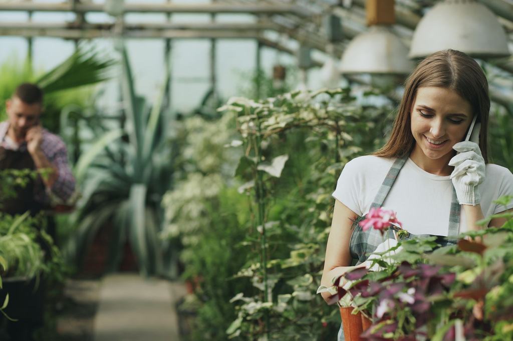 A gardener taking a phone call among plants in a greenhouse